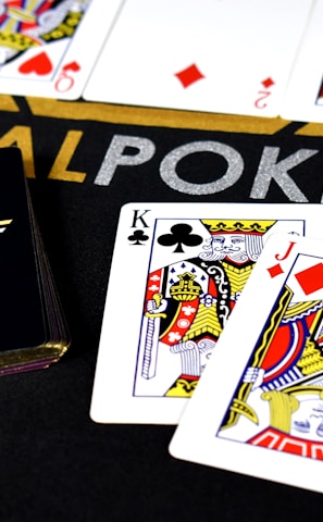 Poker-themed setup featuring a deck of cards on a table with the words 'REAL POKER' visible. Two cards, the King of Clubs and Jack of Diamonds, are prominently displayed. The design is vibrant, with detailed illustrations on the cards.