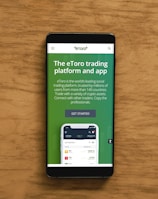 A smartphone displaying an advertisement for an online trading platform called eToro. The screen shows a green background with text promoting the platform as a leading social trading platform. A button labeled 'Get Started' is visible, along with a partial view of a mobile app screen below.