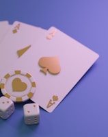 A set of playing cards displaying four aces is laid out on a surface. Alongside them, there are two poker chips with heart and diamond symbols, and three six-sided dice showing different numbers. The background is a smooth gradient of purple, creating a thematic gaming or casino atmosphere.